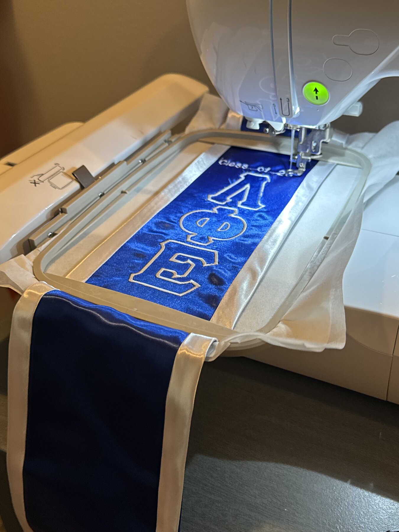Embroidery machine stitching Greek letters onto satin stole ribbon