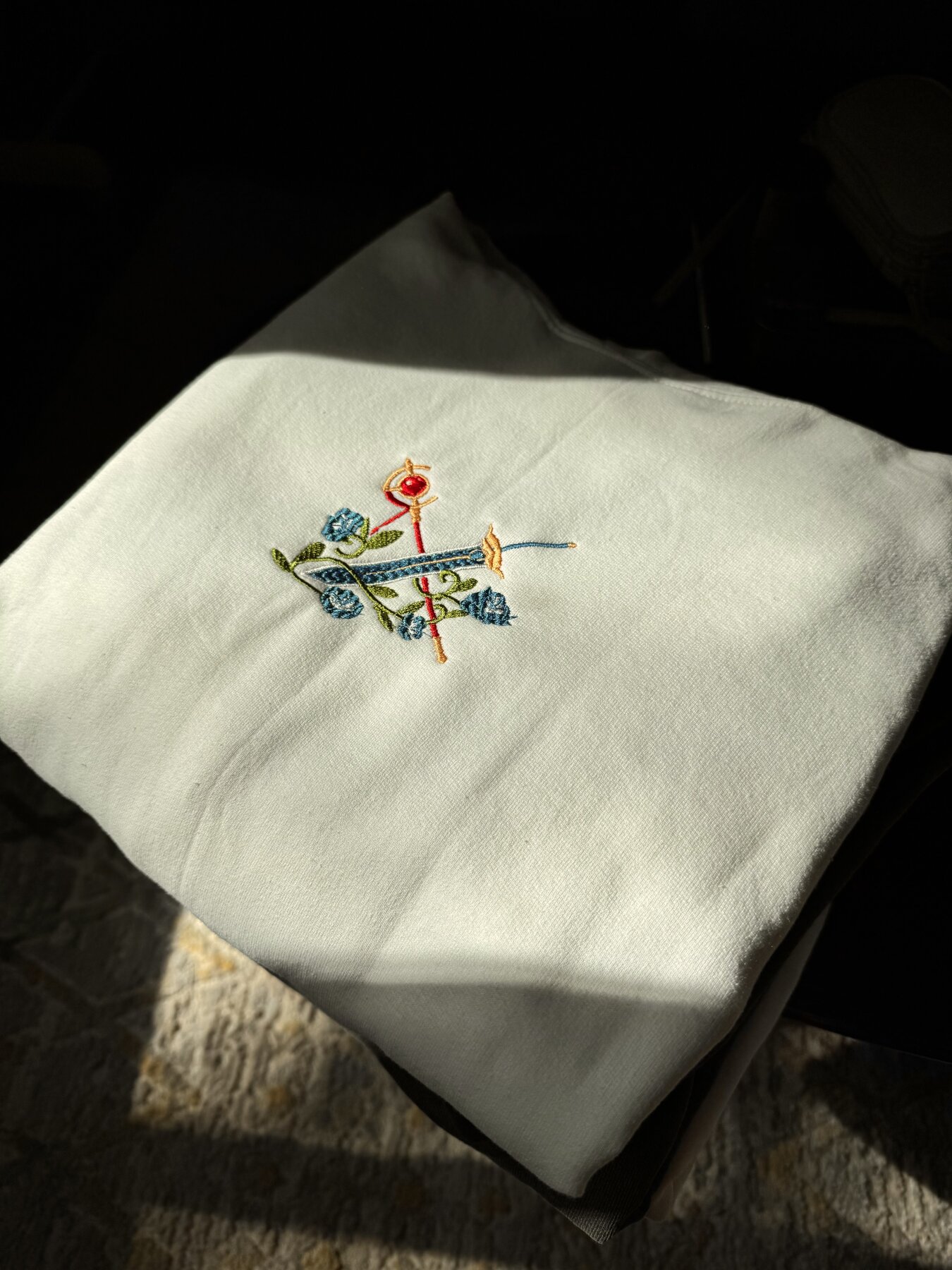 Small blue floral crest embroidered on a white tee