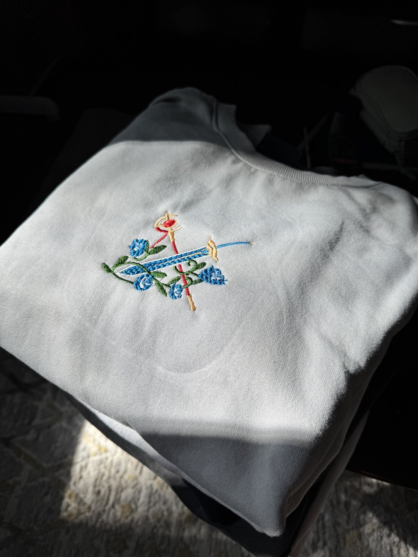 Gold necklace-style embroidery design on a grey crewneck, in packaging