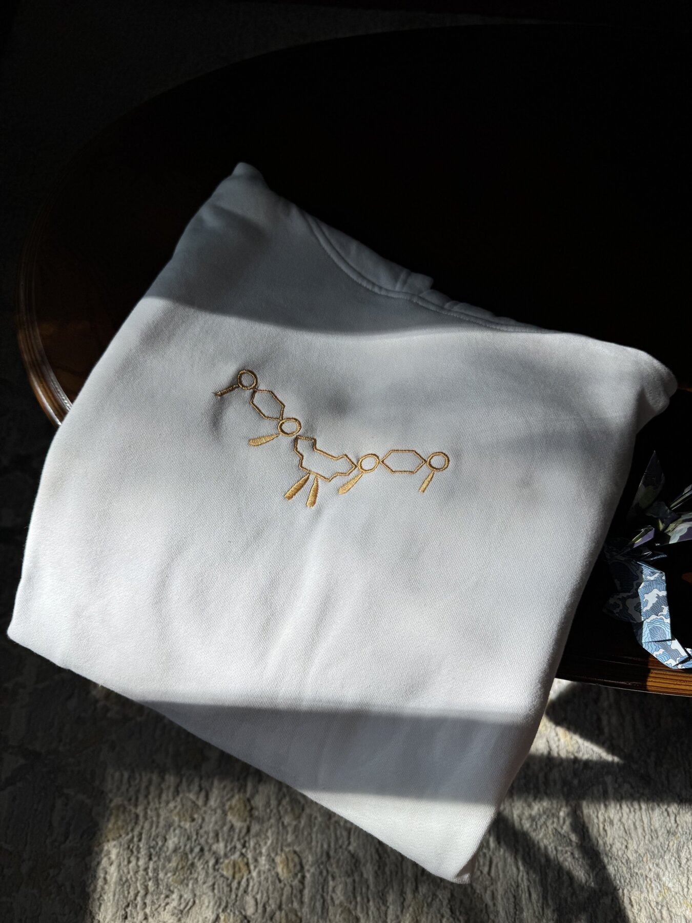 Gold wheel and wing emblem embroidered on a grey crewneck, alternate angle