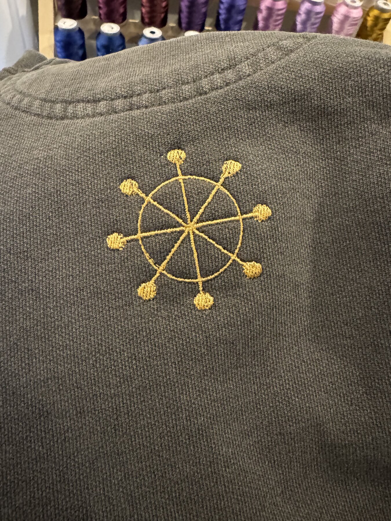 Gold wheel and wing emblem embroidered on a grey crewneck