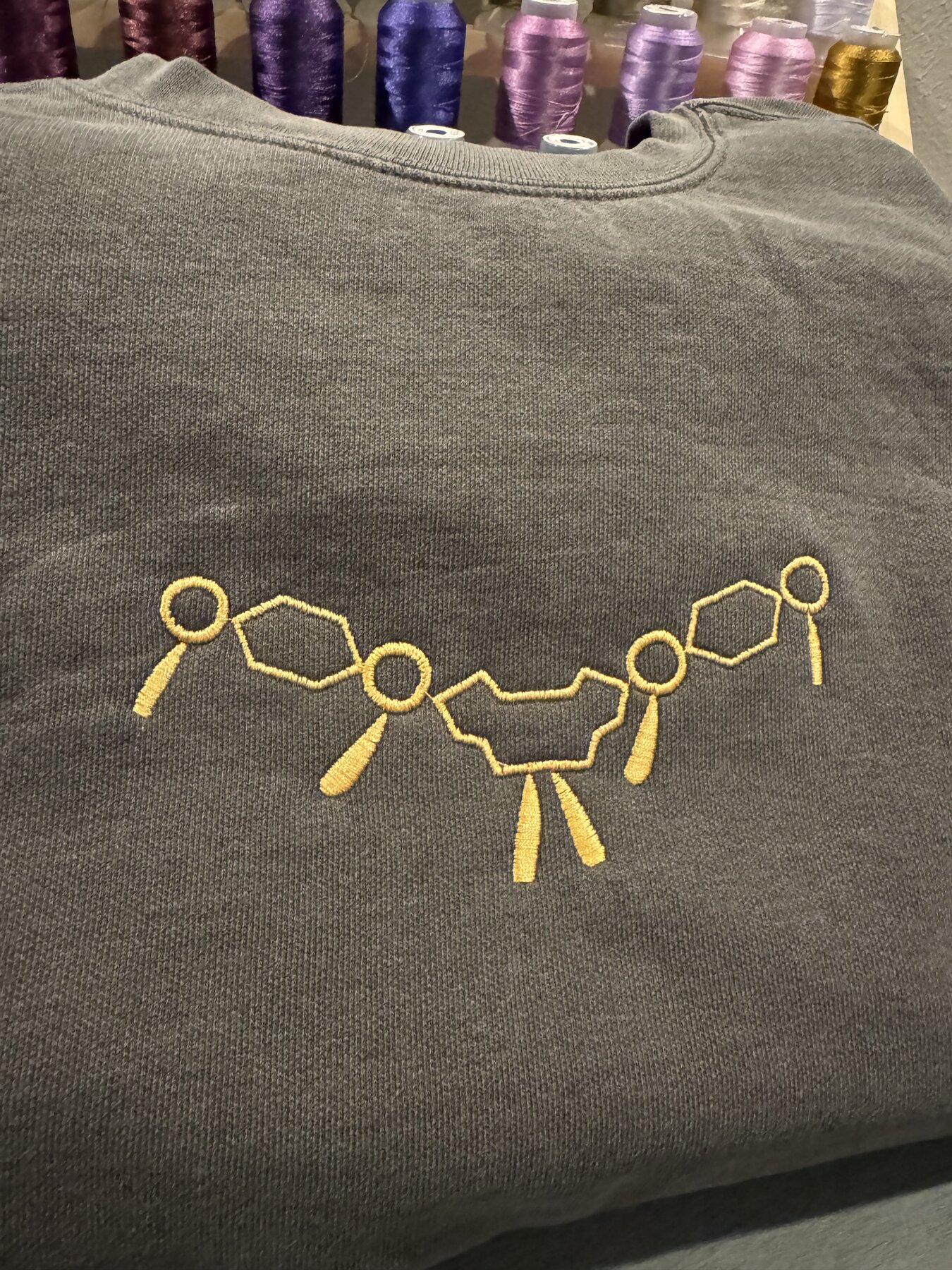 Gold necklace-style embroidery design on a grey crewneck