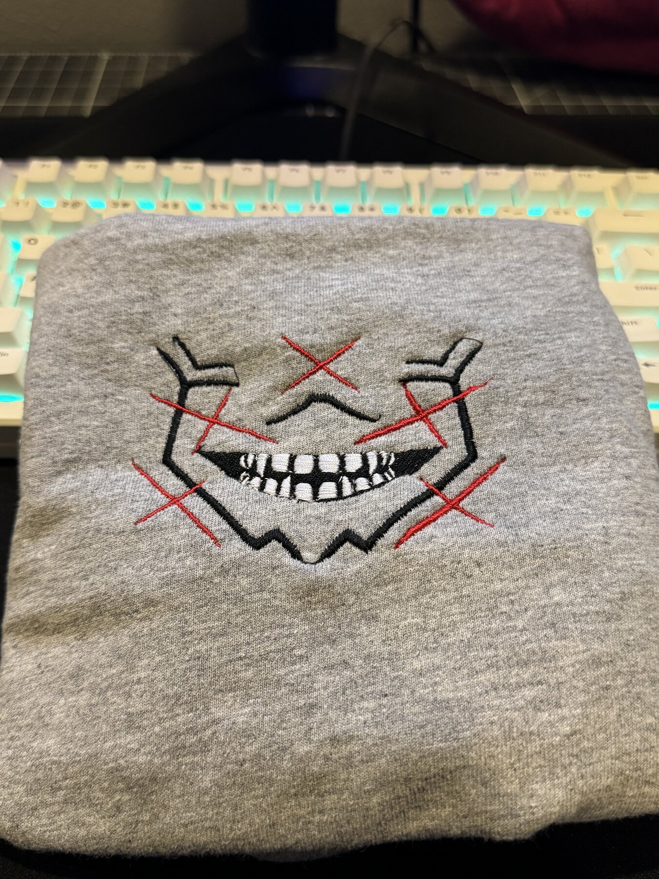 Grinning skull-style face embroidered on a grey tee