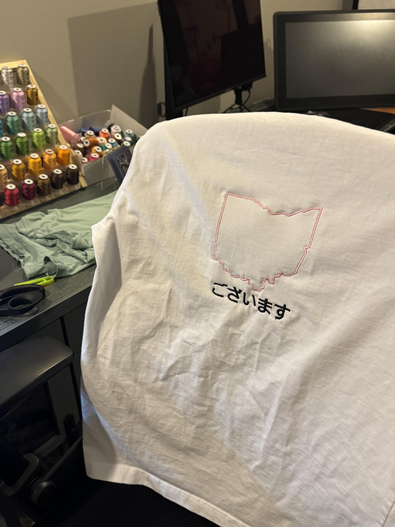 Finished embroidered tee resting on a chair beside the embroidery setup